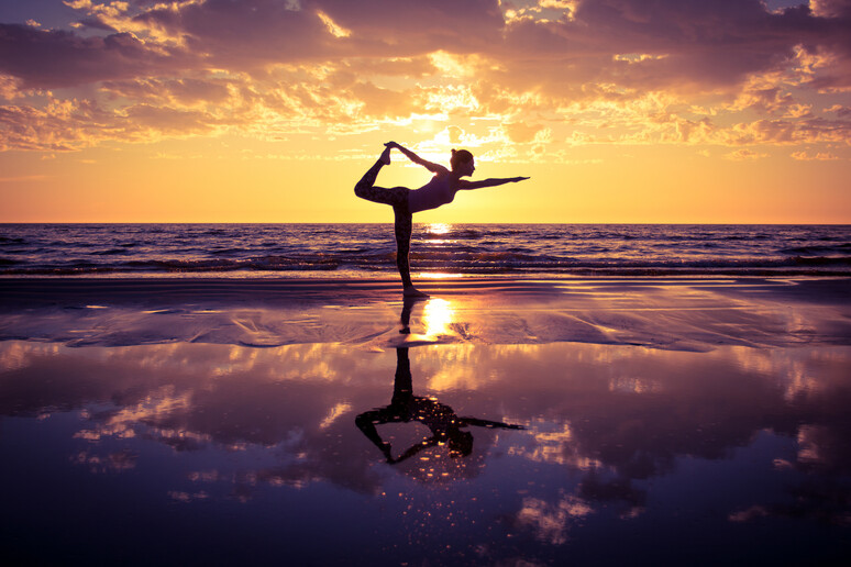 Una donna pratica yoga in spiaggia foto iStock. - RIPRODUZIONE RISERVATA